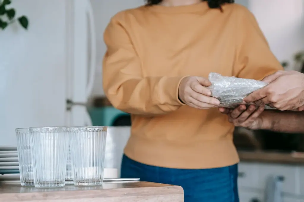 Persona envolviendo un vaso de cristal en plástico de burbujas junto a otros vasos
