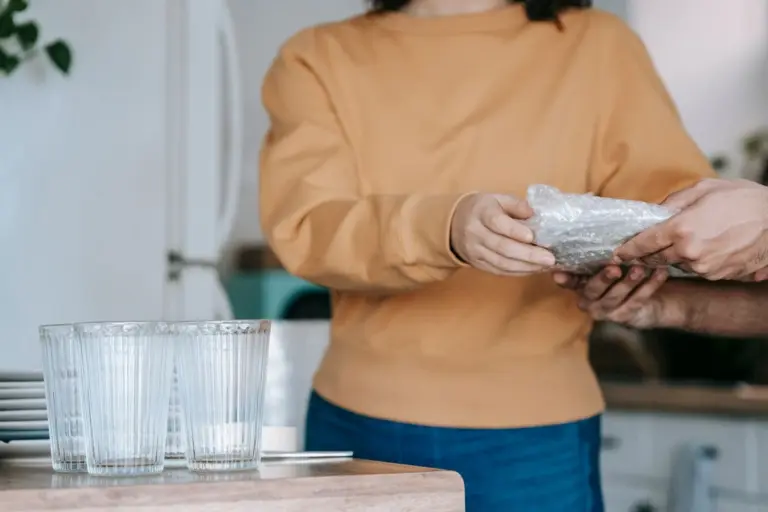 Persona envolviendo un vaso de cristal en plástico de burbujas junto a otros vasos