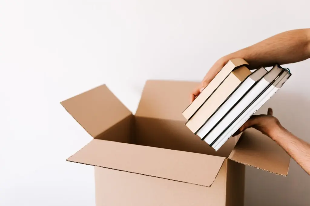 Persona metiendo una pila de libros en una caja de cartón