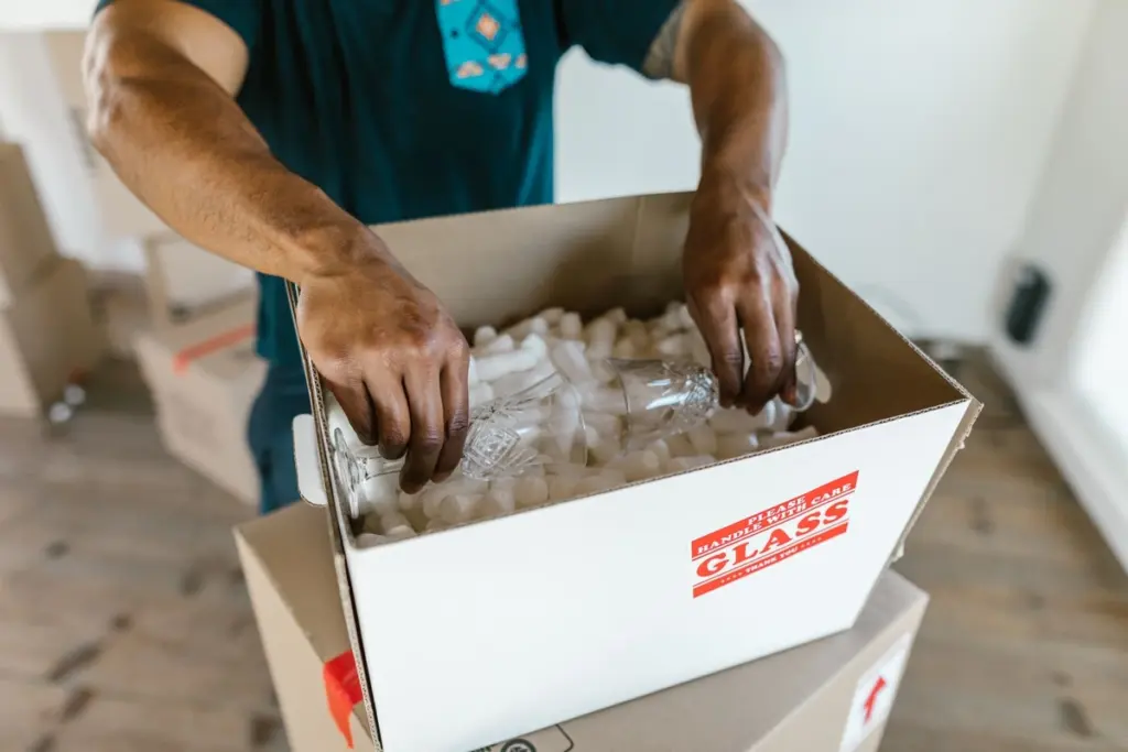 Manos colocando vasos de cristal en una caja de mudanza con relleno